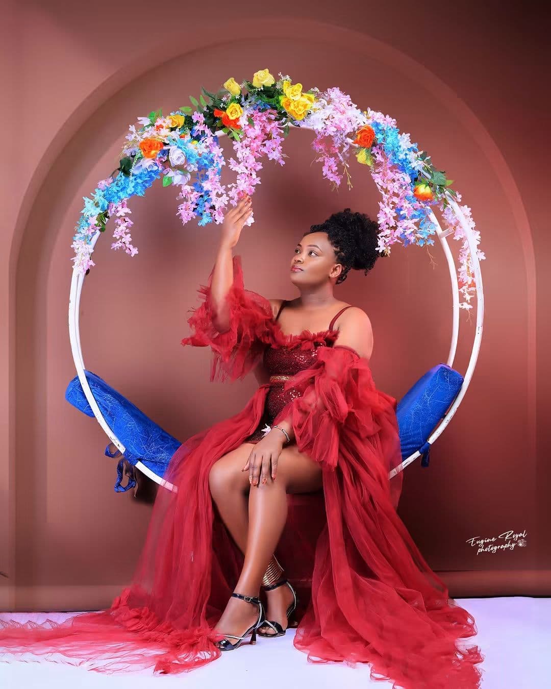 Woman in a red tulle gown seated on a swing beneath a floral hoop in a terracotta studio set
