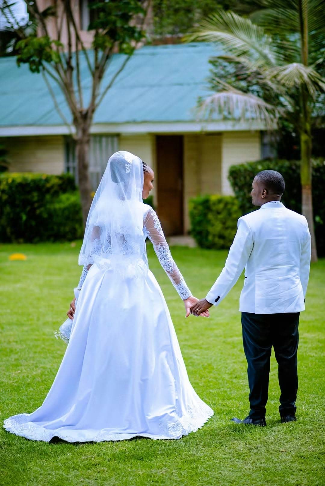Bride and groom walking hand in hand across a garden lawn